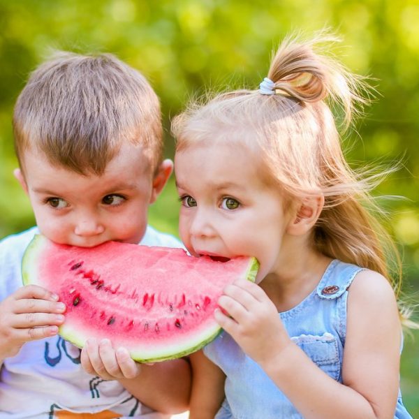 Two,Kids,Eating,One,Slice,Of,Watermelon,In,The,Garden.